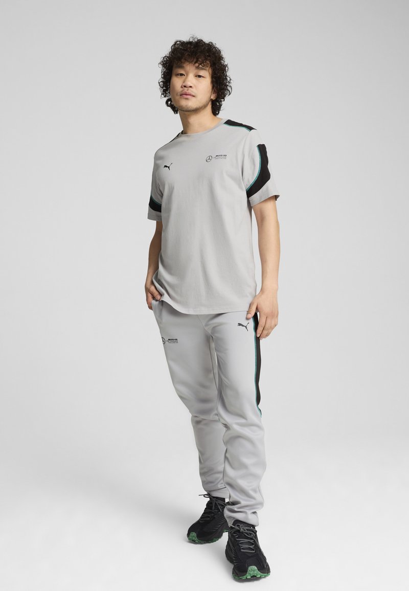 Harmaa urheilupaita ja housut mustilla ja turkooseilla yksityiskohdilla; molemmissa, niin paidassa kuin housuissa, on logot; teksturoitu kangas; rento istuvuus.