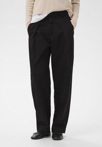Schwarze, plissierte Hose mit lockerer Passform, aus glattem Stoff. Verfügt über Seitentaschen und einen Bund mit Gürtelschlaufen.
