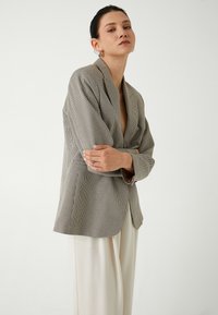 Blazer a scacchi in grigio e nero, in tessuto leggero, vestibilità su misura, rever a scatto, chiusura con un bottone, con le maniche risvoltate per un look casual.