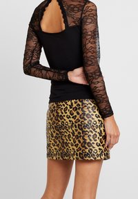 Top in pizzo nero a maniche lunghe con motivi floreali e bordi ondulati, abbinato a una gonna aderente in stampa leopardata dorata.
