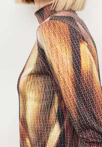 Haut à manches longues mettant en valeur un motif abstrait coloré aux teintes chaudes d'orange, de jaune et de noir, conçu avec un col haut.