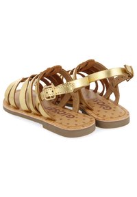 Sandali dorati e beige con più cinturini dorati, uno sfondo in suede marrone e una suola piatta. L'interno presenta motivi a stella.