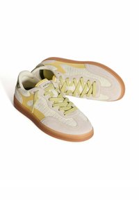 Zapatillas en beige claro con parte superior de malla y ante, acentos amarillos, punta redonda y suela de goma. Presenta cordones delgados a juego.