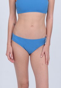 Bas de bikini bleu avec une texture lisse, un design taille basse et une couverture minimale. Le tissu semble élastique et résistant au chlore.