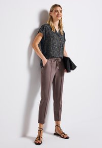 Blusa nera e dorata con motivo, scollatura a V, abbinata a pantaloni chiari beige a sigaretta con coulisse e bande laterali. Sandali neri.
