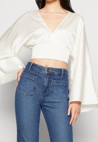 Vit satinkort topp med djup V-ringning och vida ärmar, matchad med hög midja blå denimjeans med två bakfickor.