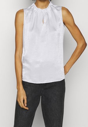 Ærmeløs hvid satinbluse med samlet halsudskæring og nøglehuludskæring, båret med sorte højttaljede jeans.