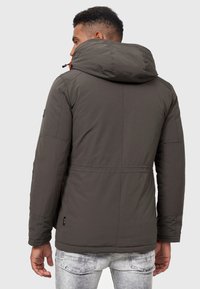 Chaqueta acolchada de color verde oscuro con capucha, que presenta una tela texturizada gris, dobladillo elástico y detalles en cordón naranja.