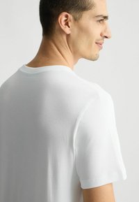 Tricou alb din bumbac, cu mâneci scurte, guler rotund și textură netedă. Cusături vizibile pe ș seams și umeri.
