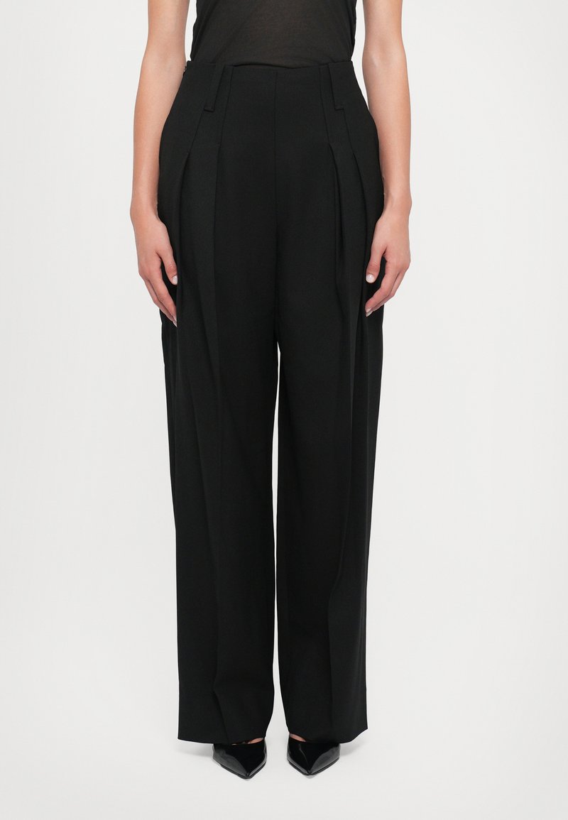 Schwarze weit geschnittene Hose mit Falten, taillierter Form, hoher Taille und einer glatten Stoffbeschaffenheit. Merkmale sind klare Linien und scharfe Falten.
