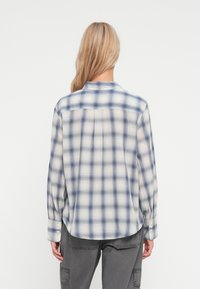 Camisa de manga longa xadrez em azul e creme, feita de tecido leve, com colarinho abotoado e bainha curva.