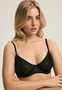 Czarny koronkowy biustonosz z miękkimi miseczkami, regulowanymi ramiączkami i falbaniastym brzegiem. Posiada misterny wzór kwiatowy oraz zapięcie na haftkę.