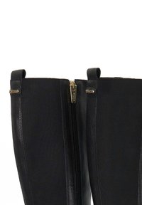 Black knee-high boots featuring a combination of smooth leather and textile, with a gold zipper detail on the front and two pull tabs.