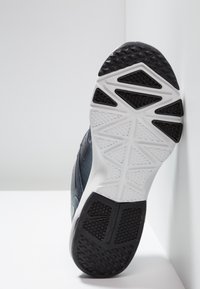 Sole of a black and white athletic shoe elevated against a white surface, showing textured tread patterns for grip.