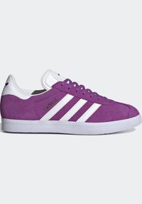 Baskets en daim violet avec des accents en cuir blanc et trois rayures blanches, présentant une semelle en caoutchouc texturé et un logo doré.