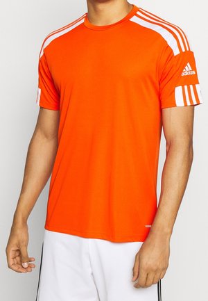Mand iført en knaldorange Adidas sportsskjorte med korte ærmer og hvide striber på skuldre og ærmer, kombineret med hvide shorts.