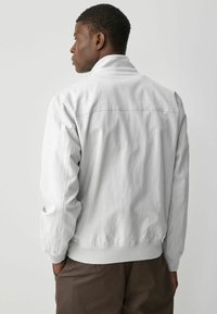 Chaqueta bomber gris claro con una textura suave, con cuello alto, puños acanalados y un diseño de espalda sólido.