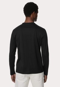Camisa de manga larga negra hecha de un tejido suave. Presenta un escote redondo y un ajuste relajado. La vista trasera muestra las costuras y una textura uniforme.