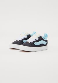Blaue und schwarze Wildledersneaker mit weißen Schnürsenkeln, die ein hellblaues Wellenmuster an den Seiten und eine weiße Gummisohle aufweisen.