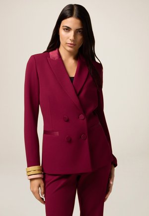 Bordeaux dubbelzijdig colbert met een satijnen revers, twee voorkielen en knoopaccenten. Gecombineerd met bijpassende slim-fit broek. Gladde textuur.