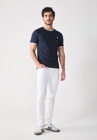 Mornarska majica kratkih rukava s bijelim ovratnikom i akcentima na rukavima, u kombinaciji sa slim-fit bijelim trapericama i sivim/crnim tenisicama.