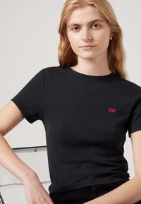 Tricou negru cu mânecă scurtă, fabricat din material ribbed, având un logo mic roșu Levi's pe piept. Textură netedă și decupaj clasic la guler.