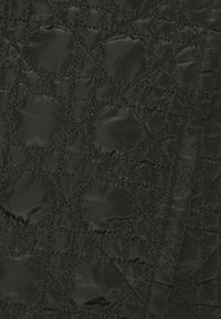 Tessuto nero trapuntato con un motivo a diamante, caratterizzato da una texture lucida e accenti circolari. La superficie mostra una leggera lucentezza e dettagli di cucitura.