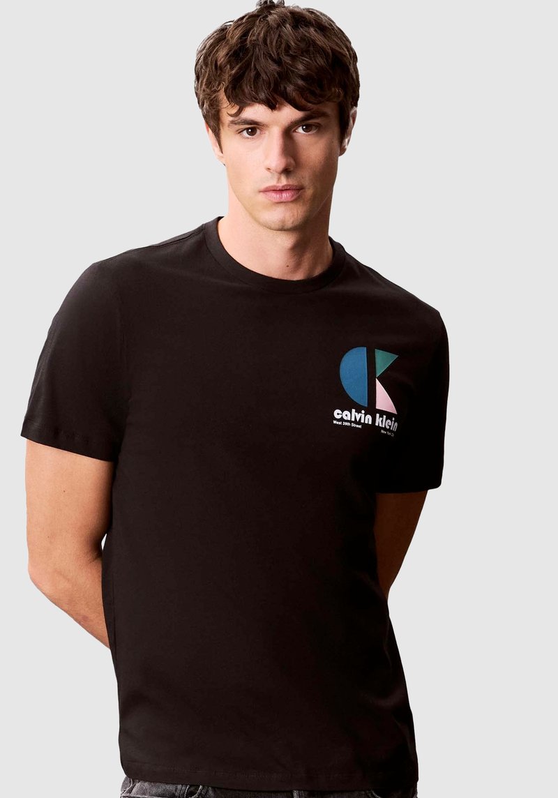 Camiseta de algodón negra con cuello redondo, mangas cortas y un diseño frontal con logo en azul, rosa y blanco con letras en contraste.