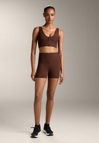 Top court côtelé marron avec détail de boutons, associé à un short taille haute assorti. Le modèle porte des chaussures de sport noires sur un fond neutre.