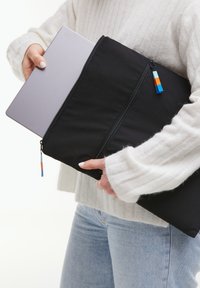 Svart laptopfodral i tyg, med dubbla dragkedjor, färgglada dragkedjedragare och en slät yta, som rymmer en silverfärgad laptop.
