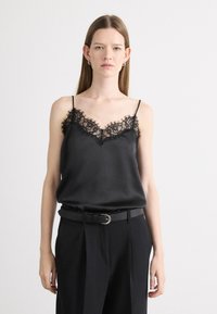 Svart satin cami-top med blonder trim langs halslinjen og kantene. Har tynne justerbare stropper og en avslappet passform. Brukt med høytlivede svarte bukser.