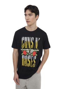 T-shirt in cotone nero con un design grafico che presenta "GUNS N' ROSES," rose e revolver in giallo, rosso e verde. Maniche corte, collo rotondo.