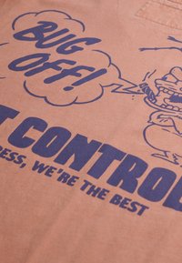 Camiseta de algodón color durazno con texto azul destacado: "¡Lárgate!" y "CONTROL DE PESTES", con imágenes de dibujos animados y diseño de burbuja de diálogo.