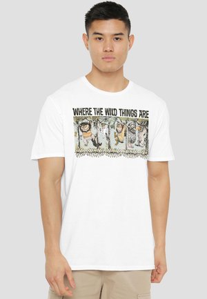 Young man wearing a white T-shirt with "Where the Wild Things Are" text and illustrated wild creatures hanging from tree branches.