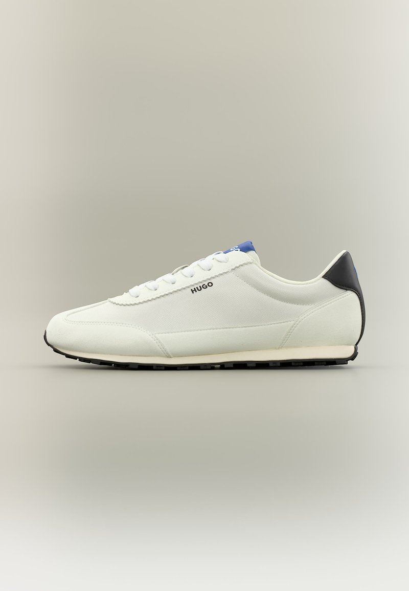 Biały niski sneaker z czarnym obcasem, niebieskim detalem na języku, białymi sznurowadłami i logo „HUGO” po boku, widoczny z profilu.