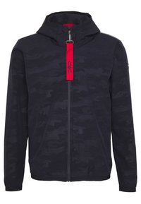 Hættetrøje i mørk marineblå med camouflage mønster. Har en rød lynlåstræk og elastiske manchetter. Lavet af letvægtsstof.