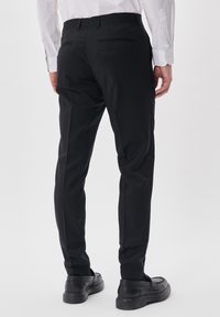 Black tailored trousers with a slim fit, featuring two back pockets and a smooth texture. Paired with black loafers and a white shirt.