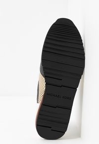 Black sole of a sneaker with textured grooves and "MICHAEL KORS" logo, part of a mesh and metallic rose gold upper visible.