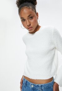 Witte, gestructureerde trui met een ronde hals en korte pasvorm, gecombineerd met blauwe denim jeans. Beschikt over lange mouwen en een zachte, pluizige oppervlakte.
