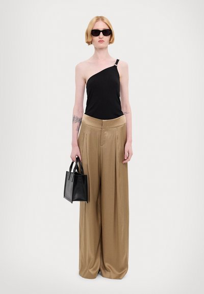 Asymmetrisch zwart geribbeld topje, beige geplisseerde wijde broek, en kleine zwarte handtas. Model met zonnebril, minimale accessoires.
