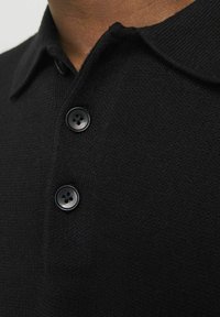 Polo shirt tricotat negru cu guler clasic și trei nasturi negri. Textura pare moale și uniformă, potrivită pentru îmbrăcăminte casual.