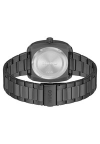 Reloj de acero inoxidable negro con caja cuadrada, pulsera a juego y hardware pulido. Presenta un fondo redondo de metal cepillado con logo.