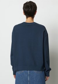 Sudadera azul marino de corte relajado, con cuello redondo y hombros caídos. Textura suave y puños acanalados; combinada con una falda de jean.