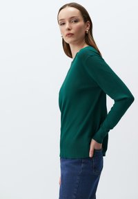 Zielony sweter z długim rękawem, okrągłym dekoltem, ściągaczem u dołu oraz teksturowanym materiałem, połączony z dżinsami o wysokim stanie.