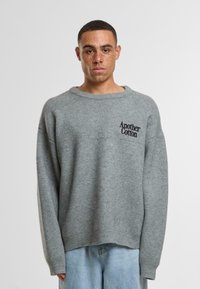 Maglione grigio, oversize, realizzato in materiale morbido, con colletto e polsini a costine, con "Another Cotton" ricamato in nero sul petto.