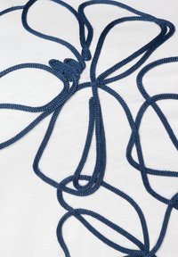 Tissu blanc avec un cordon tressé bleu foncé formant un motif floral avec des boucles et des nœuds. Apparence texturée en raison du matériau tissé.