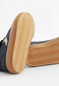 Baskets en suède bleu marine avec une semelle en caoutchouc à motifs en chevron. Les accents comprennent un logo beige sur le côté et des détails de couture.