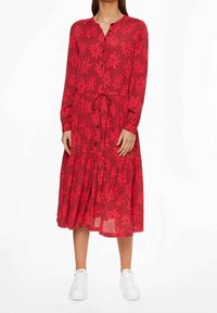 Abito lungo a maniche lunghe con stampe floreali rosse, con bottoni frontali, vita aderente e gonna a strati, abbinato a sneaker bianche.