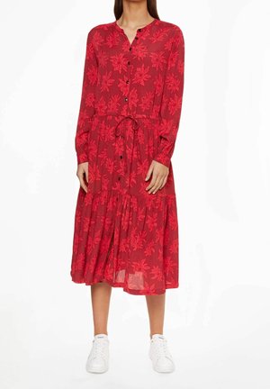 Rode bloemen jurk met lange mouwen, een knoopsluiting aan de voorkant, een cinched taille en een gelaagd rokk ontwerp, gecombineerd met witte sneakers.