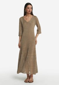 Strick-Maxi-Kleid in Hellbraun mit V-Ausschnitt, dreiviertel Ärmeln und komplizierten geometrischen Mustern am Saum. Getragen mit flachen Sandalen.